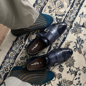 Peut inclure: Une paire de chaussures en cuir bleu fonc&eacute; avec une boucle de fermeture. Les chaussures sont port&eacute;es avec des chaussettes ray&eacute;es dans les tons bleu sarcelle et or.