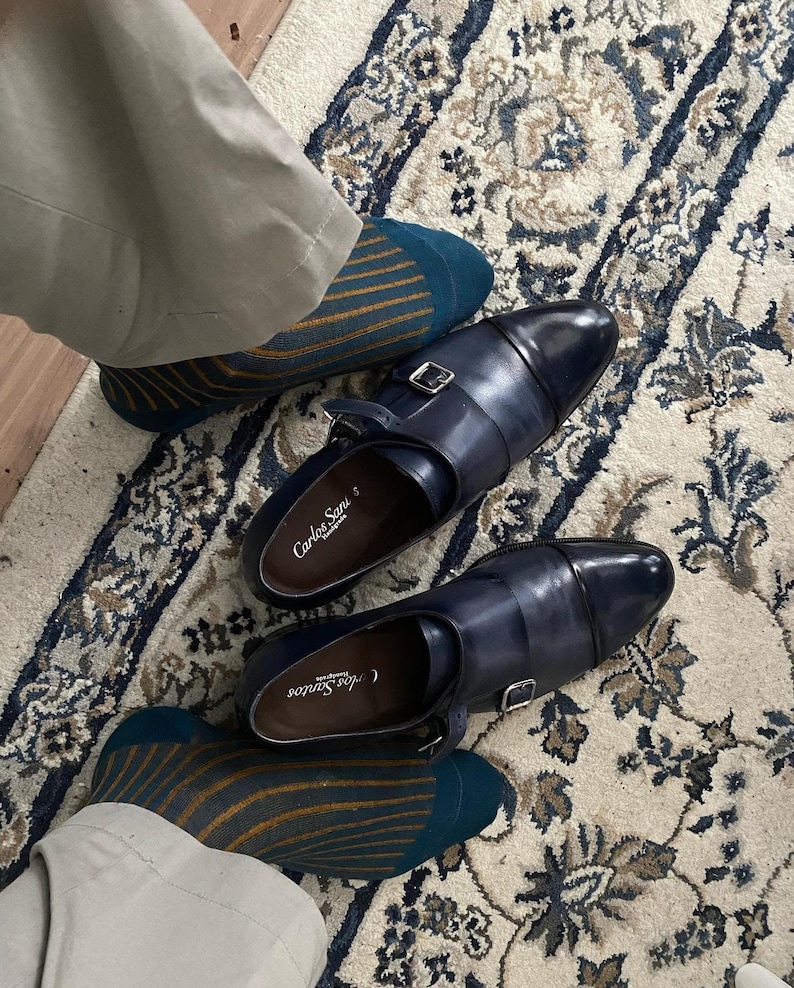 Peut inclure: Une paire de chaussures en cuir bleu fonc&eacute; avec une boucle de fermeture. Les chaussures sont port&eacute;es avec des chaussettes ray&eacute;es dans les tons bleu sarcelle et or.