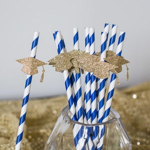 May include: Blue and white striped paper straws with gold glitter graduation caps attached. The straws are in a clear glass jar.