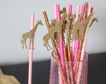 May include: A collection of pink and gold paper straws with glittery gold giraffe cutouts. The straws are arranged in a clear, textured glass. The giraffe toppers add a playful touch to the party supplies.