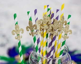 May include: A bunch of green, purple, and yellow striped paper straws with gold glitter fleur-de-lis decorations. The straws are in a clear glass jar.