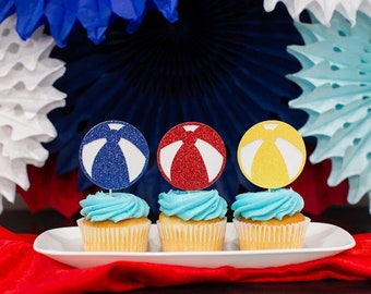 May include: Three cupcakes with blue frosting topped with glitter beach ball cupcake toppers in blue, red, and yellow.