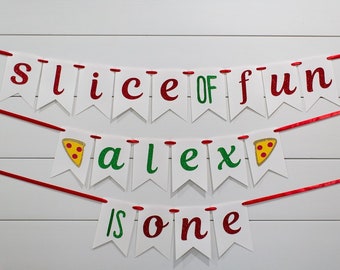 Könnte beinhalten: Ein weißes Banner mit roten und grünen Glitzerbuchstaben, auf dem "slice of fun alex is one" steht, mit Pizzastückchen-Bildern auf dem Banner.