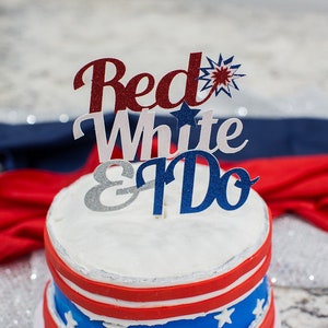 Pode incluir: Um bolo de casamento branco com cobertura vermelha, branca e azul e um topo de bolo que diz "Red White & Do".