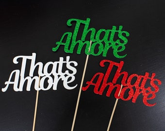 May include: Three "That's Amore" signs, one in white glitter, one in red glitter, and one in green glitter. Each sign is attached to a wooden stick.