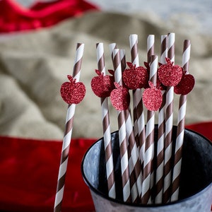 May include: A close-up of a group of brown and white striped paper straws with red glitter apple decorations. The straws are in a silver metal bucket.