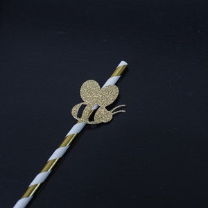 May include: A white and gold striped paper straw with a gold glitter bee cutout attached to the top.