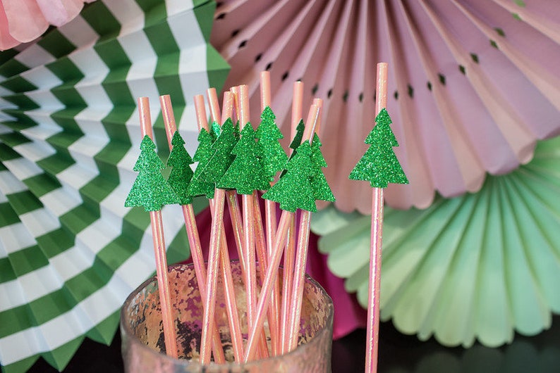 May include: A bunch of pink and white striped paper straws with green glitter Christmas tree toppers. The straws are in a clear glass jar.