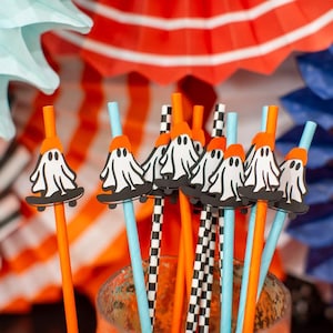 May include: A collection of Halloween-themed straws with ghost-shaped decorations on skateboards. The straws are orange, blue, and black and white checkered. Colorful paper fans in the background add to the festive atmosphere.