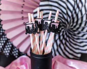Puede incluir: Pajitas rayadas de color rosa y blanco con adornos de caldero de purpurina negra en un recipiente negro.