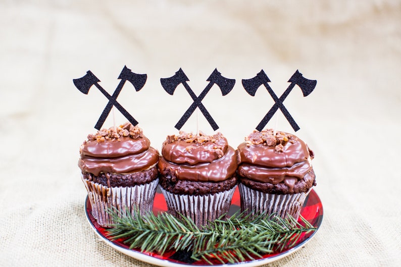 Pu&ograve; includere: Tre cupcake al cioccolato con glassa al cioccolato e noci tritate in cima. Ogni cupcake &egrave; sormontato da un topper a forma di ascia di carta nera.