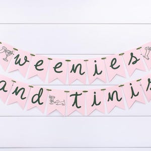 May include: Pink banner with the words "weenies and tinis" in dark green script. Each pennant is pink and has a small illustration of a dachshund and a martini glass. The banner is strung on green ribbon.