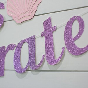 May include: Purple glitter banner with the words "Let's Celebrate" on a white wood background.