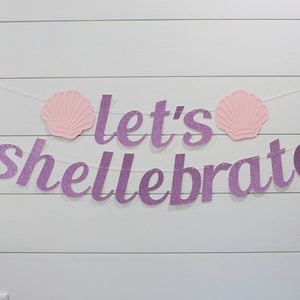 May include: Purple glitter banner with the text "Let's Shellebrate" and two pink seashells on a white wood background.