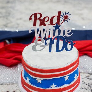 Pode incluir: Um bolo branco de dois andares decorado com listras vermelhas e azuis e estrelas brancas. O bolo &eacute; coberto com um topo de bolo vermelho, branco e azul que diz "Red White & I Do."