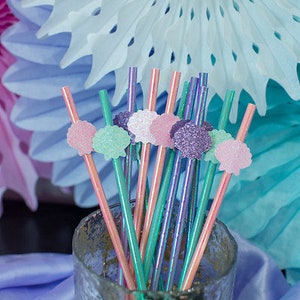 May include: A glass jar filled with colorful iridescent straws with decorative seashell toppers in pink, green, and purple. The straws are perfect for a mermaid-themed party.