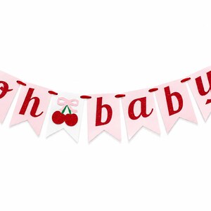 May include: A decorative banner featuring light pink pennants strung on a red cord. The letters spell out "oh baby" in a glittery red font. A white pennant in the center displays two red cherries with a small light pink bow above them.