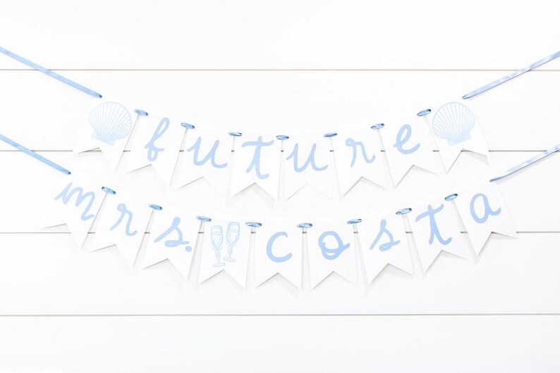Op de afbeelding: Een decoratieve banner met twee lagen bestaande uit witte wimpels aan een lichtblauw lint. De bovenste rij spelt future met schelpenafbeeldingen en de onderste rij spelt mrs. costa met afbeeldingen van champagneglazen in lichtblauw.