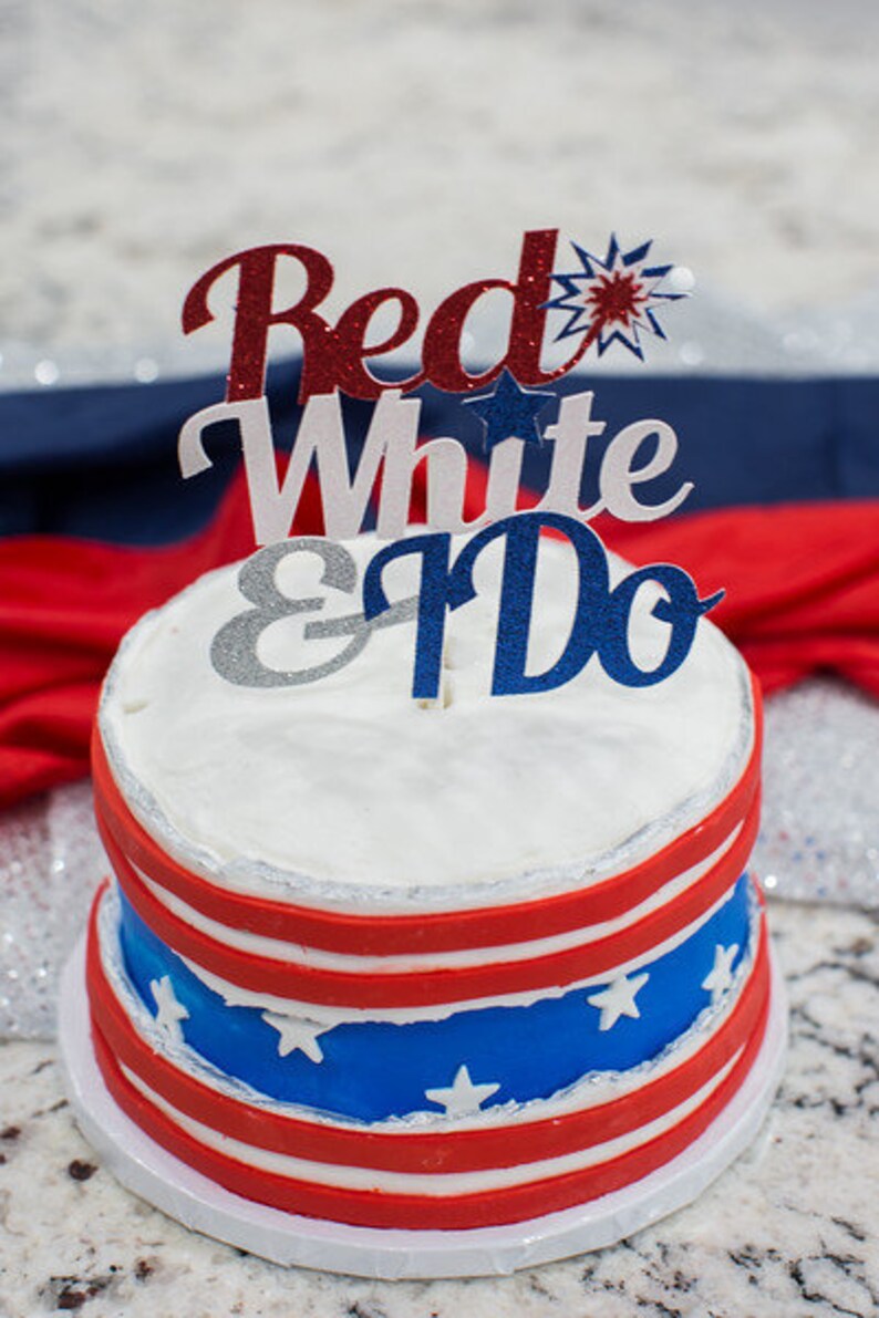 Pode incluir: Um bolo de casamento de dois andares decorado em vermelho, branco e azul com um topo que diz "Red White & Do".