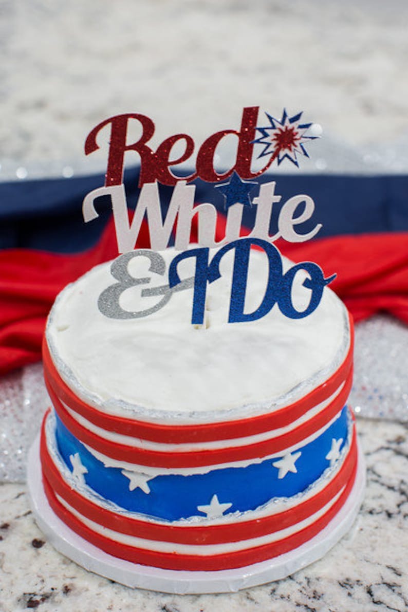 Pode incluir: Um bolo de casamento de dois andares decorado em vermelho, branco e azul com um topo que diz "Red White & Do".