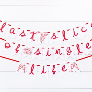 May include: A white banner with red text that reads "last slice of single life." The banner includes pizza and champagne glass illustrations. The banner is strung with red ribbon against a white wooden background.