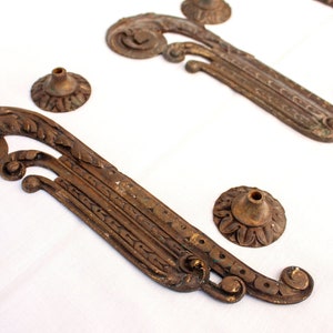 Può includere: Quattro pezzi decorativi in metallo dorato antico con disegni ornamentali. I pezzi hanno la forma di rotoli con dettagli intricati e hanno un aspetto usurato e invecchiato.