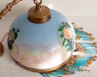 May include: A vintage blue glass lampshade with a painted floral design and a brass chain and fixture. The lampshade is surrounded by a fringe of blue and gold beads.