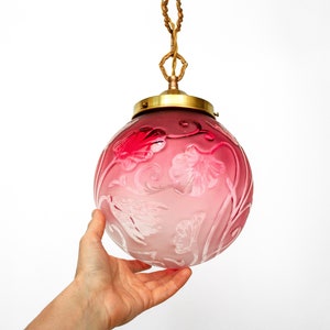 May include: A pink glass pendant light with a floral design. The light is hanging from a chain and has a brass fixture.