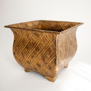 May include: A square, decorative planter with a textured, golden-brown finish. The planter has a flared rim and sits on four small feet. The surface features a crisscross pattern, adding visual interest. Ideal for indoor or outdoor use.