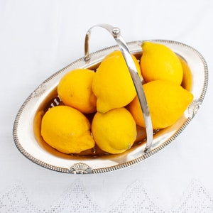 May include: A silver serving dish with a handle, filled with yellow lemons.