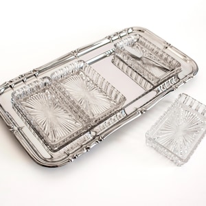 May include: A rectangular silver-toned metal serving tray with a decorative rim, featuring three clear glass rectangular dishes with a sunburst pattern. One additional matching glass dish is placed separately beside the tray.