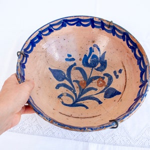 May include: A large, round, ceramic plate with a blue and white floral design. The plate has a crack in the glaze and is hanging from two metal hooks.