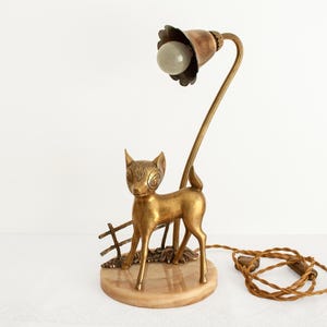 Puede incluir: Una lámpara de mesa de latón con una figura de ciervo y una pantalla de vidrio blanco. La lámpara está sobre una base de mármol.