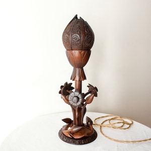 May include: A dark brown wooden table lamp with a carved flower design. The lampshade is shaped like a flower bud and has intricate carvings.