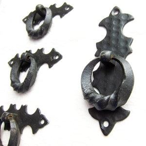 Puede incluir: Cuatro tiradores de cajón de metal negro con un diseño de anillo retorcido. Los tiradores tienen un diseño decorativo y ornamentado con bordes puntiagudos.