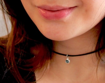 May include: A close-up of a woman wearing a black choker necklace with a small silver pendant. The necklace is simple and elegant, and the pendant is a small circle.
