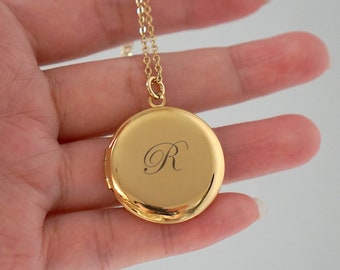 May include: Gold locket necklace with a round pendant engraved with the letter "R".