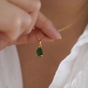 May include: A gold chain necklace with a teardrop-shaped green gemstone pendant.