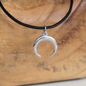 May include: A silver crescent moon pendant hangs from a black leather cord necklace.