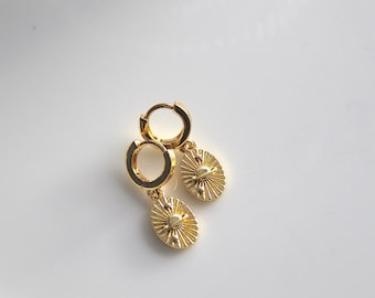 May include: A pair of gold hoop earrings with a small, round, sun-shaped charm hanging from each hoop.