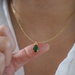 May include: A gold chain necklace with a small teardrop-shaped green gemstone pendant.