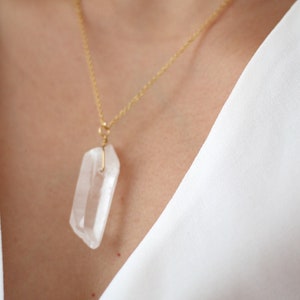 May include: A gold chain necklace with a clear quartz crystal pendant.