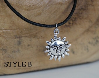 May include: A silver sun pendant necklace with a face on the sun, hanging from a black leather cord. The necklace is on a wooden surface with the text "STYLE B" printed on it.