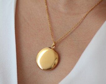 May include: A gold chain necklace with a round gold locket pendant.