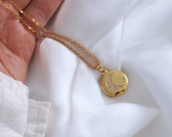 May include: A gold chain necklace with a crescent moon pendant. The pendant is adorned with small, sparkling stones.