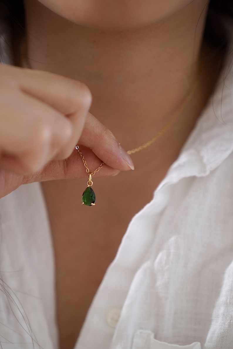 May include: A gold chain necklace with a teardrop-shaped green gemstone pendant.