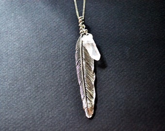 May include: A silver feather pendant necklace with a clear quartz crystal charm. The necklace is on a black background.