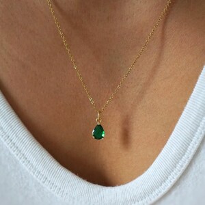 May include: A gold chain necklace with a teardrop-shaped green gemstone pendant.