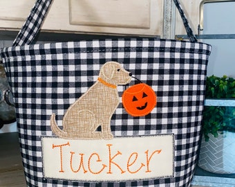 Könnte beinhalten: Schwarzer und weißer karierter Stoff-Trick-or-Treat-Eimer mit einem braunen Hund, der einen Kürbis hält. Der Eimer hat ein Namensschild mit der Aufschrift "Tucker".