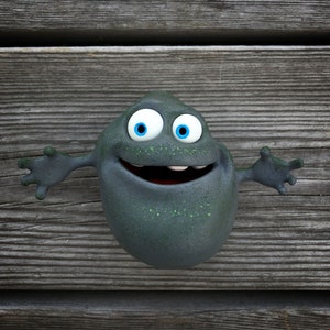 Puede incluir: Un monstruo de dibujos animados con grandes ojos azules y una boca abierta de par en par, sonriendo con los dientes. El monstruo es gris con manchas verdes y tiene dos brazos extendidos.